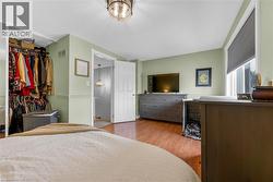 Bedroom featuring wood-finish flooring, a ceiling-mounted light fixture, and a large window with a roller shade - 