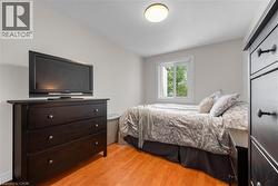 Bedroom featuring a bright window with white trim, wood-finish flooring, and a ceiling-mounted light fixture - 