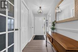 Foyer featuring wood-finish flooring, white paneled doors, two contemporary light fixtures, and a decorative wall mirror - 