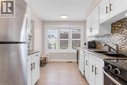 Galley kitchen featuring white cabinetry with matte black hardware, mosaic tile backsplash, black double basin sink, and a stainless steel refrigerator - 