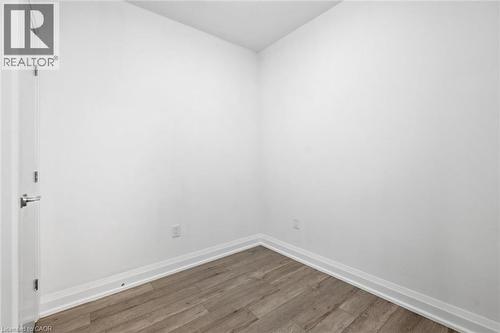 Room featuring neutral white walls, wood-finish flooring, and white baseboards - 212 King William Street Unit# 418, Hamilton, ON 