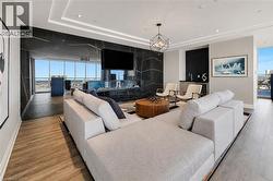 Spacious living area featuring expansive windows, wood-finish flooring, a contemporary fireplace with a dark stone surround, a wet bar, and recessed lighting - 