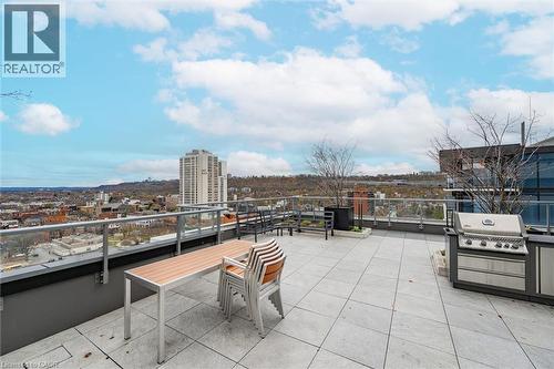 Expansive rooftop terrace featuring large format paver flooring, glass railing, built-in outdoor kitchen with grill, and cityscape backdrop - 212 King William Street Unit# 418, Hamilton, ON 