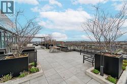 Expansive rooftop terrace with large format paver flooring, multiple planter beds, glass railings, and a pergola structure - 