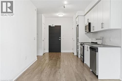 Modern kitchen with white cabinetry, stainless steel appliances, dark countertops, and a subtle tiled backsplash - 212 King William Street Unit# 418, Hamilton, ON 