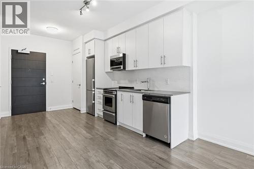 Modern kitchen featuring white cabinetry, stainless steel appliances, and a mosaic tile backsplash - 212 King William Street Unit# 418, Hamilton, ON 