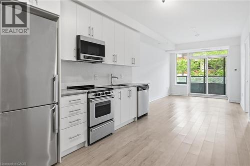Kitchenette featuring stainless steel appliances, white cabinetry, a light-toned backsplash, and a light wood-finish floor - 212 King William Street Unit# 418, Hamilton, ON 
