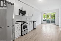 Kitchenette featuring stainless steel appliances, white cabinetry, a light-toned backsplash, and a light wood-finish floor - 