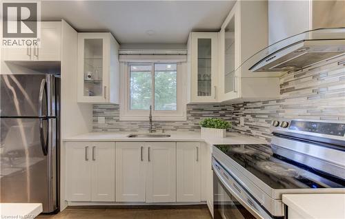 Modern kitchen featuring white shaker cabinetry, stainless steel appliances, a multi-tone tile backsplash, and a built-in range hood - 619 Forest Hill Drive, Kitchener, ON 