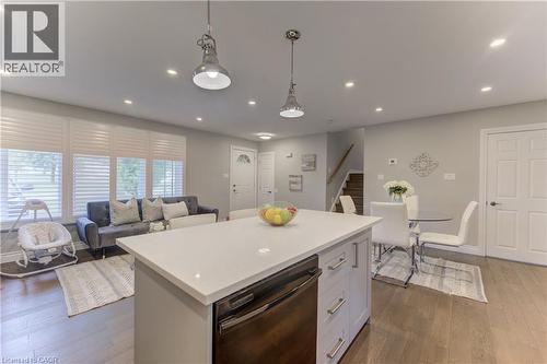 Open-concept living area featuring a kitchen island with a light-toned countertop, recessed lighting, wood-finish flooring, and multiple windows with horizontal blinds - 619 Forest Hill Drive, Kitchener, ON 