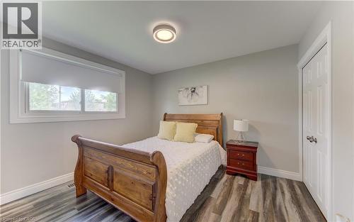 Bedroom featuring wood-finish flooring, a contemporary ceiling light fixture, a window with white trim, and a paneled white door - 619 Forest Hill Drive, Kitchener, ON 