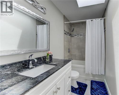 Bathroom featuring a dark speckled countertop vanity with an undermount sink, a framed mirror, and a tub with a tiled surround - 619 Forest Hill Drive, Kitchener, ON 