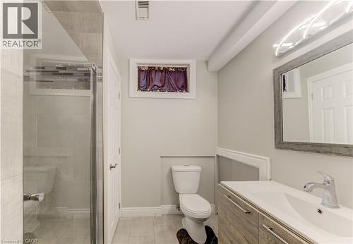 Contemporary bathroom featuring a glass-enclosed shower with tile surround and mosaic accent, a wood-finish vanity with an integrated sink, a framed mirror with modern lighting, and tile flooring - 619 Forest Hill Drive, Kitchener, ON 