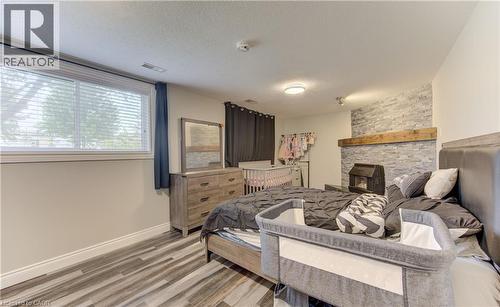Bedroom featuring wood-finish flooring, a stone-accented wall with a wood mantel, a window with blinds, and recessed lighting - 619 Forest Hill Drive, Kitchener, ON 