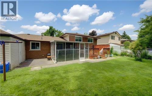 Rear exterior featuring a screened-in sunroom, multi-level wood deck, and a large grassy yard - 619 Forest Hill Drive, Kitchener, ON 