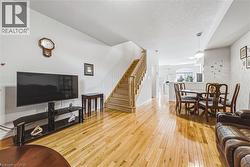 Bright open-concept living area featuring wood-finish flooring, a wood staircase with balusters, and a dining area with a pendant light fixture - 