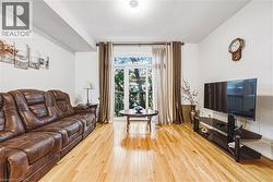 Bright living area featuring wood-finish flooring, a large window with exterior foliage, and white walls - 