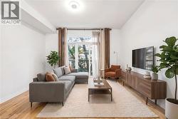 Spacious living area featuring light wood-finish flooring, a large glass-paned door opening to a balcony, high ceilings, and a built-in media console - 