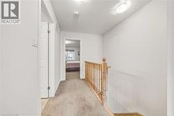 Carpeted hallway featuring light wood banister, white walls, and flush-mount ceiling lighting - 