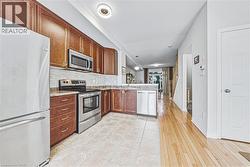 Kitchen featuring warm wood-finish cabinetry, stainless steel appliances, a tile backsplash, and stone-look countertops - 