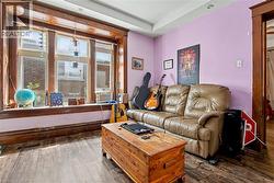 Main Floor Living room featuring wood-finish flooring, a large multi-pane window with wood trim, and a high ceiling - 