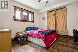 Main Floor Bedroom featuring wood-finish flooring, a ceiling fan, and a three-panel window with wood trim - 