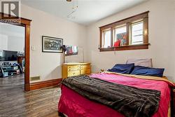 Main Floor Bedroom featuring wood-finish flooring, a window with wood trim, and a doorway with wood casing - 
