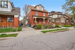 Brick exterior with a covered front porch featuring decorative railing, a paved driveway, and mature landscaping - 