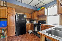 Kitchen featuring wood cabinetry, a double basin stainless steel sink, a tiled countertop, and a black range - 