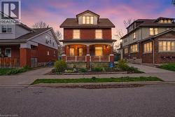 Brick-clad residence featuring a covered front porch with decorative railing, multiple window dormers, and a gabled roofline - 