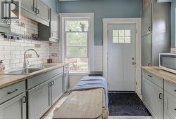 Kitchen featuring light gray cabinetry, wood-finish countertops, and a subway tile backsplash with decorative accents - 