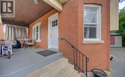 Brick facade residence featuring a covered porch with a wood-finish ceiling, concrete entry steps, a black metal handrail, and white-framed windows with stone sills - 