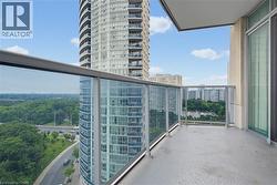 Private balcony with glass railings, concrete flooring, and sliding glass door access, featuring an urban landscape with visible roadways and surrounding high-rise buildings - 