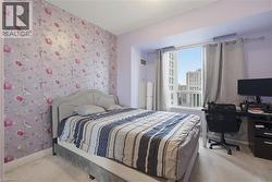 Bedroom featuring a prominent window, patterned accent wall, light-colored carpeting, and painted walls - 