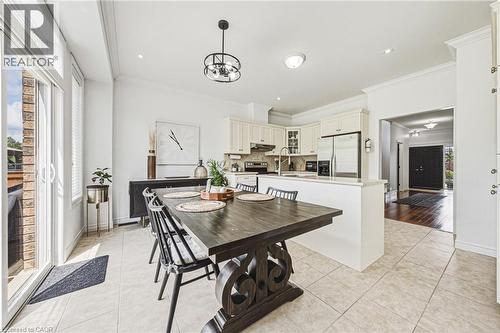 Open-concept kitchen and dining area featuring light-toned tile flooring, recessed lighting, crown molding, and a sliding glass door leading to an exterior space - 20 Degrow Crescent, Binbrook, ON 