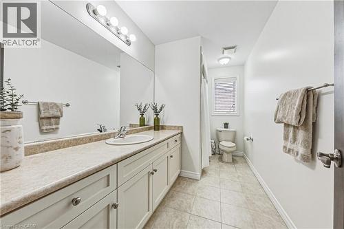 Bathroom featuring an extended vanity with an integrated sink, ample storage cabinetry, a full-width mirror, and a toilet with a window - 20 Degrow Crescent, Binbrook, ON 