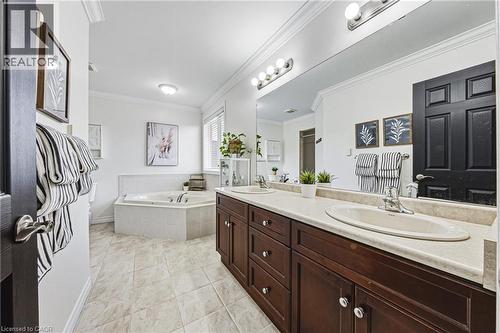Bathroom featuring a dual vanity with dark wood-finish cabinetry and light-toned countertops, a built-in corner soaking tub, a tiled floor, and crown molding - 20 Degrow Crescent, Binbrook, ON 