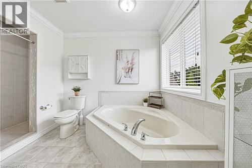 Corner soaking tub with tile surround, separate shower enclosure, tiled flooring, white vanity cabinet, and window with blinds - 20 Degrow Crescent, Binbrook, ON 
