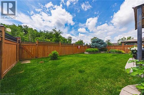 Expansive lawn area featuring a wooden fence with black decorative top accents, a raised garden bed with mature plantings, and a concrete patio section - 20 Degrow Crescent, Binbrook, ON 