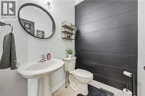 Pedestal sink with chrome faucet, complemented by a black oval-framed mirror and wall-mounted shelving - 20 Degrow Crescent, Binbrook, ON 