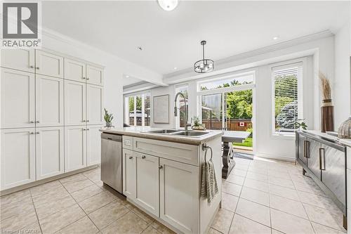 Kitchen featuring an island with dual sinks, extensive white cabinetry, stainless steel dishwasher, and tile flooring - 20 Degrow Crescent, Binbrook, ON 