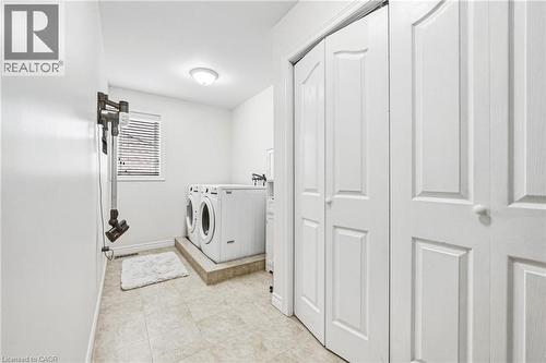 Dedicated laundry area featuring front-loading appliances, neutral tile flooring, and a window with blinds - 20 Degrow Crescent, Binbrook, ON 