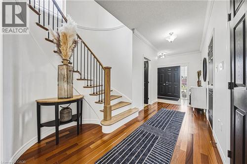 Foyer featuring rich wood-finish flooring, a curved staircase with black metal balusters and wood handrail, white walls, and a black paneled double entry door with transom - 20 Degrow Crescent, Binbrook, ON 