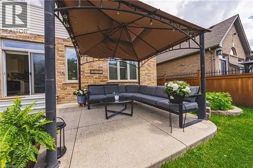 Exterior patio featuring a metal gazebo with a fabric canopy, concrete slab, brick facade, sliding glass door, and green lawn - 20 Degrow Crescent, Binbrook, ON 
