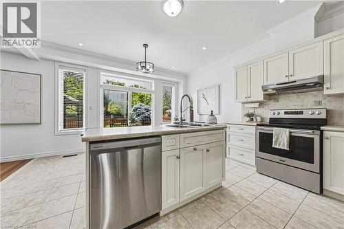 Bright kitchen featuring white cabinetry, stainless steel appliances, a center island with a sink, tile flooring, and ample natural light from multiple windows - 20 Degrow Crescent, Binbrook, ON 