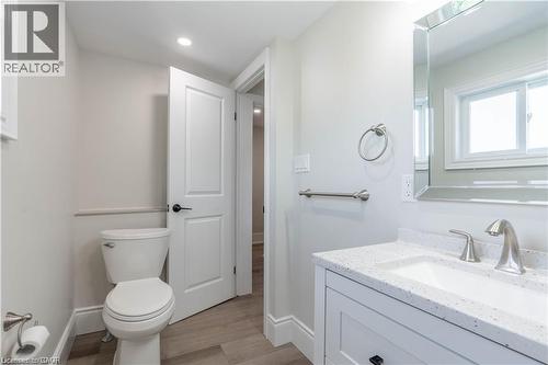 Bathroom featuring a modern vanity with a white countertop and integrated sink, a large mirrored medicine cabinet, brushed nickel fixtures, and wood-finish flooring - 66 Queen Street W, Cambridge, ON 