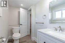 Bathroom featuring a modern vanity with a white countertop and integrated sink, a large mirrored medicine cabinet, brushed nickel fixtures, and wood-finish flooring - 