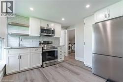 Modern kitchen featuring white shaker cabinetry, stainless steel appliances, granite countertops, and wood-finish flooring - 