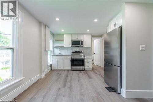 Modern kitchen featuring stainless steel appliances, white cabinetry with dark hardware, subway tile backsplash, recessed lighting, and wood-finish flooring - 66 Queen Street W, Cambridge, ON 