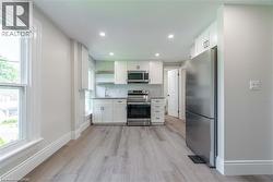 Modern kitchen featuring stainless steel appliances, white cabinetry with dark hardware, subway tile backsplash, recessed lighting, and wood-finish flooring - 